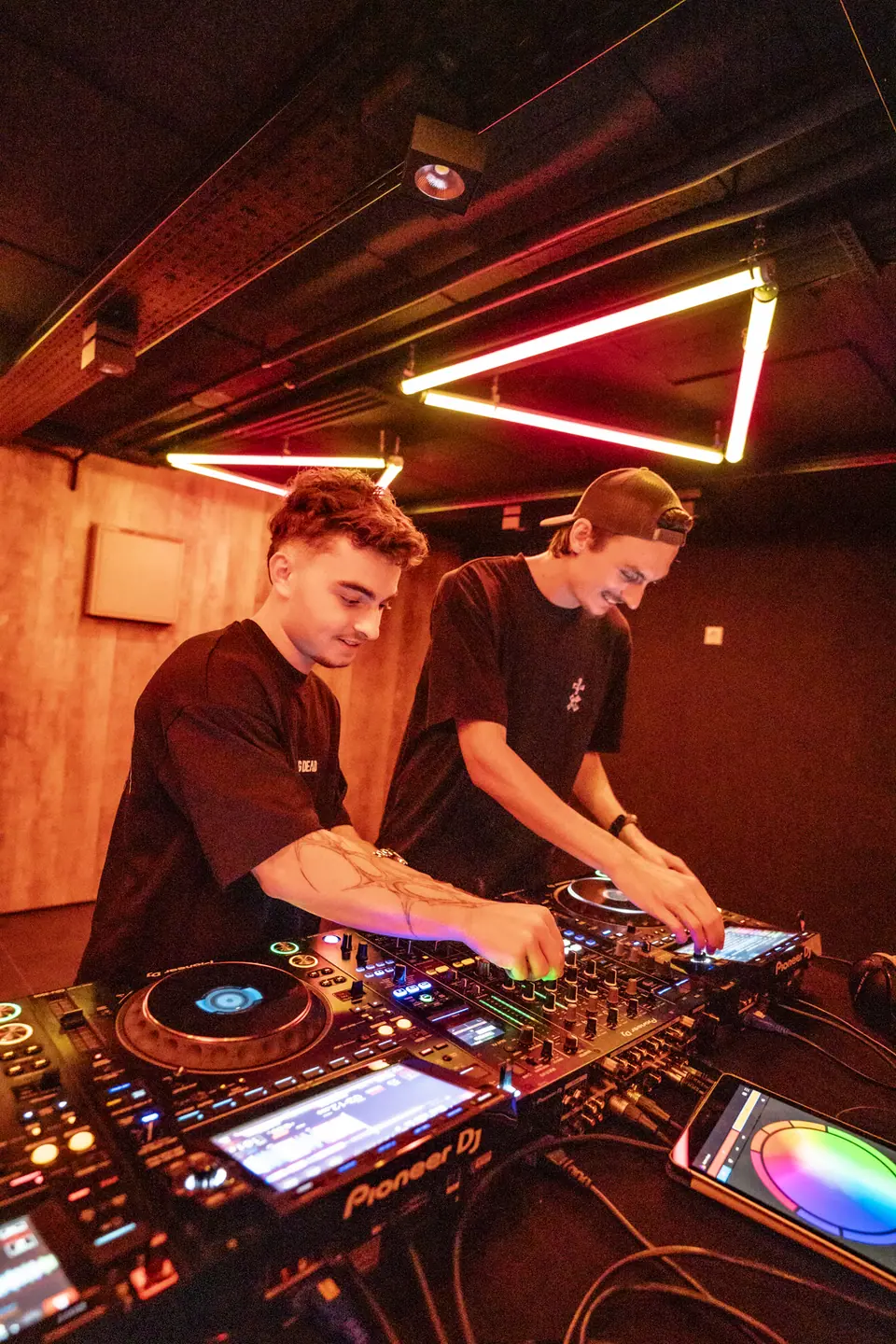 Deux DJ aux platines, néons rouges au plafond